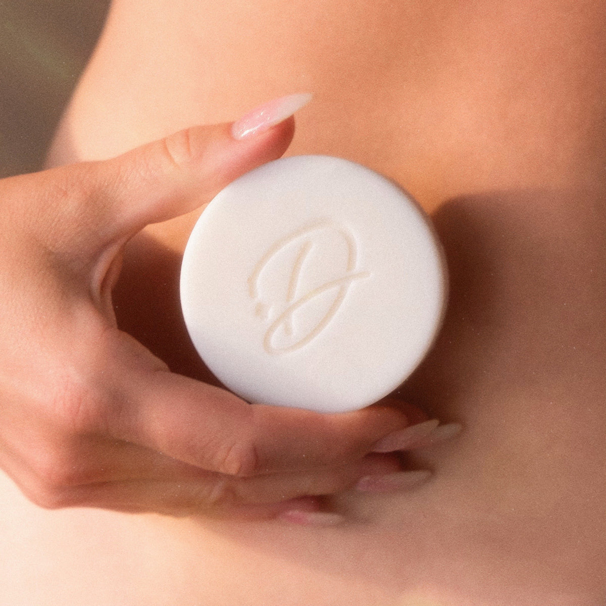 Hands holding a white Darlin’ lotion bar embossed with a script D.